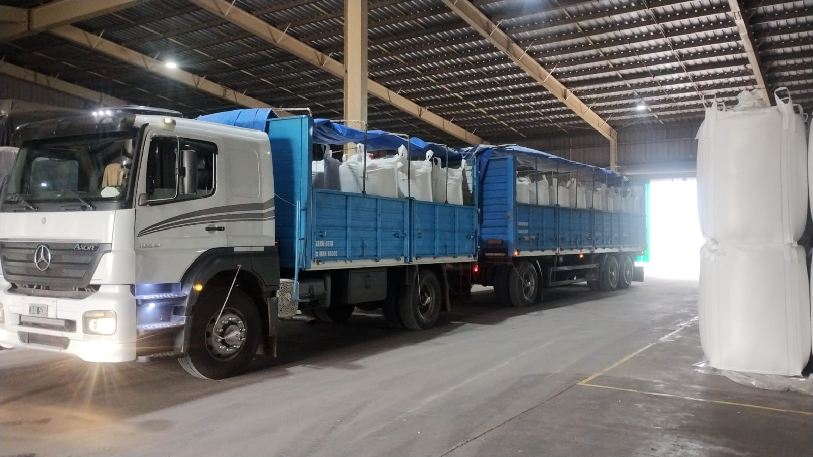 Camión con acoplado de Transporte PETI cargado con big bags en galpón